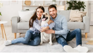 Un homme et une femme souriants aux côtés de leur chien dans un salon.